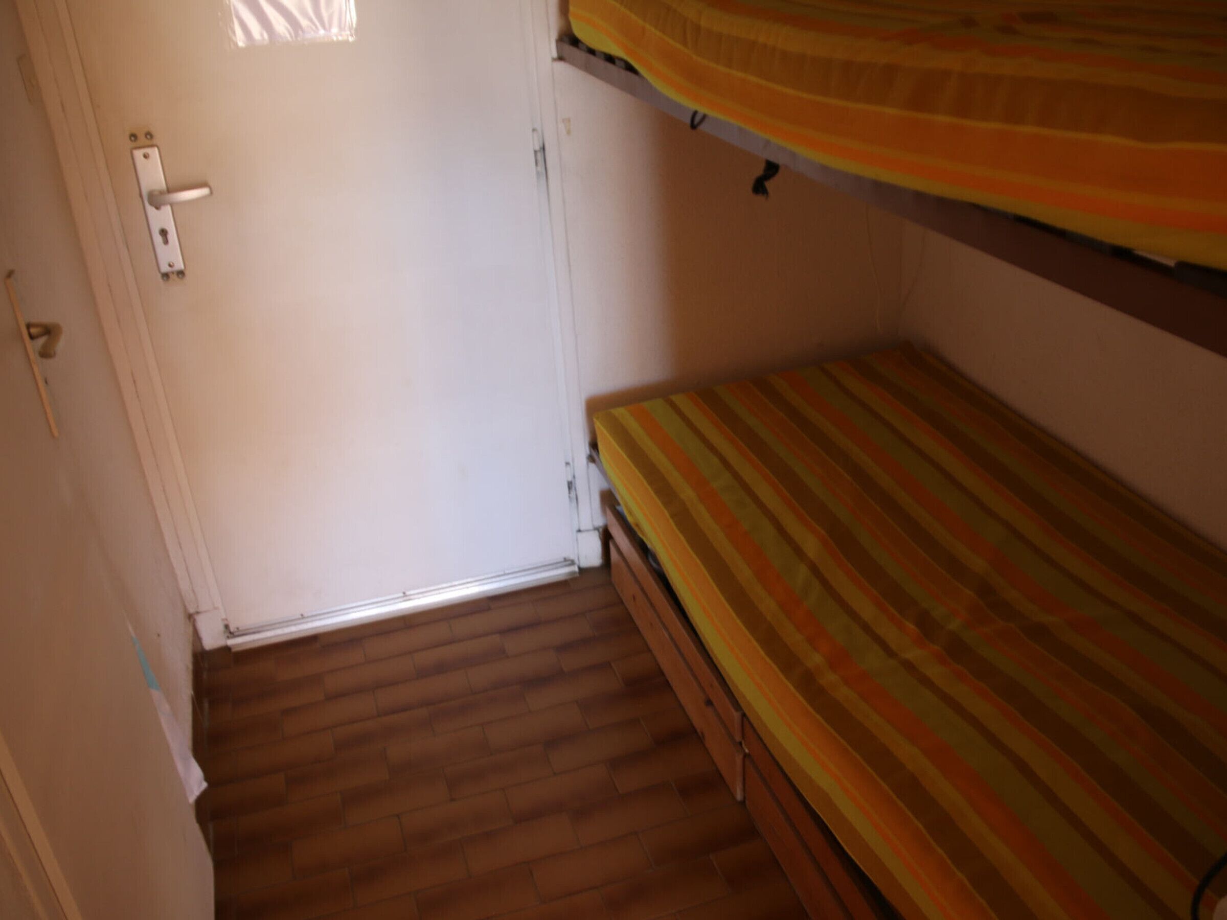 A room with a wooden floor, a door with a handle, and a bunk bed with a striped mattress.