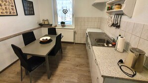 Kompakti keittiö, jossa on ruokapöytä, tuolit, sydämenmuotoinen koriste ikkunassa sekä työtaso, jossa on vedenkeitin ja keittiövälineet.