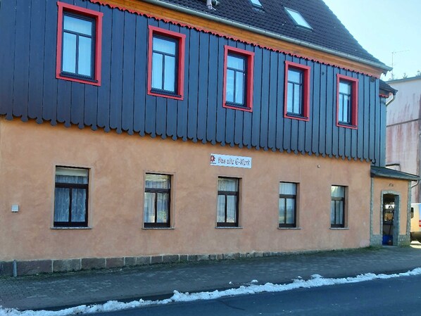 A building with a dark blue facade and red window frames, featuring a sign that reads "Das alte E-Werk."