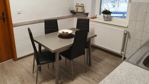Ruokailutilassa on pöytä, tuoleja ja kulho ruokaa. Seinällä on kaksi kehystettyä kasvitieteellistä taulua.