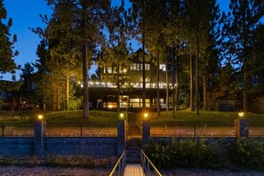 Een gebouw met twee verdiepingen en een overdekt terras, omgeven door bomen en een geplaveid pad naar de ingang.
