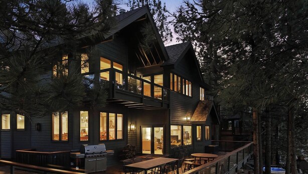 A multi-story cabin with large windows, a deck, and a grill area.