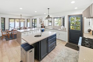 A modern kitchen with a central island, large windows, and a view of the outdoors.