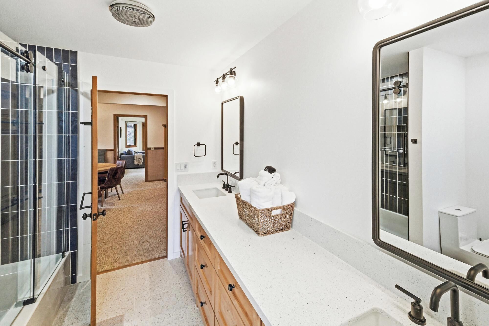 A modern bathroom with a large mirror, two sinks, a shower, and a walk-in closet.