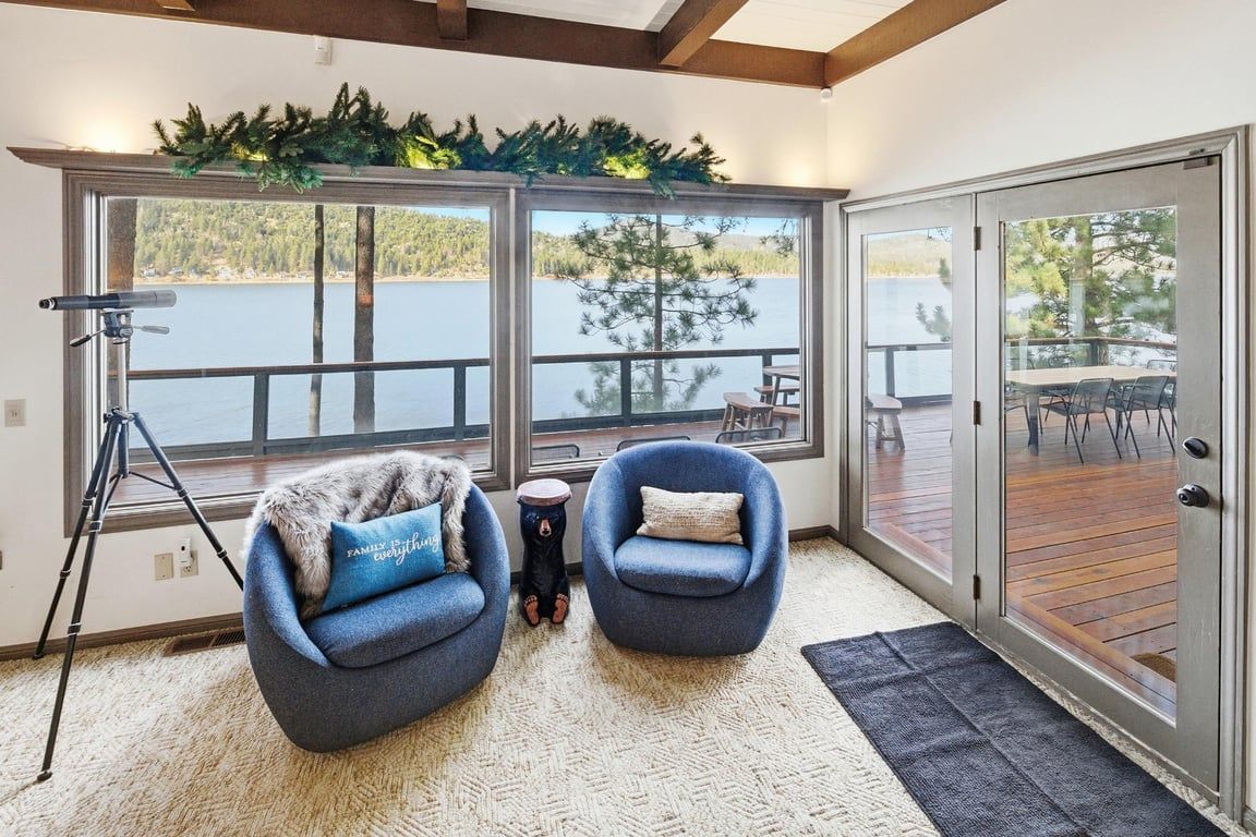 A room with two blue armchairs, a tripod, and a view of a lake through large windows.