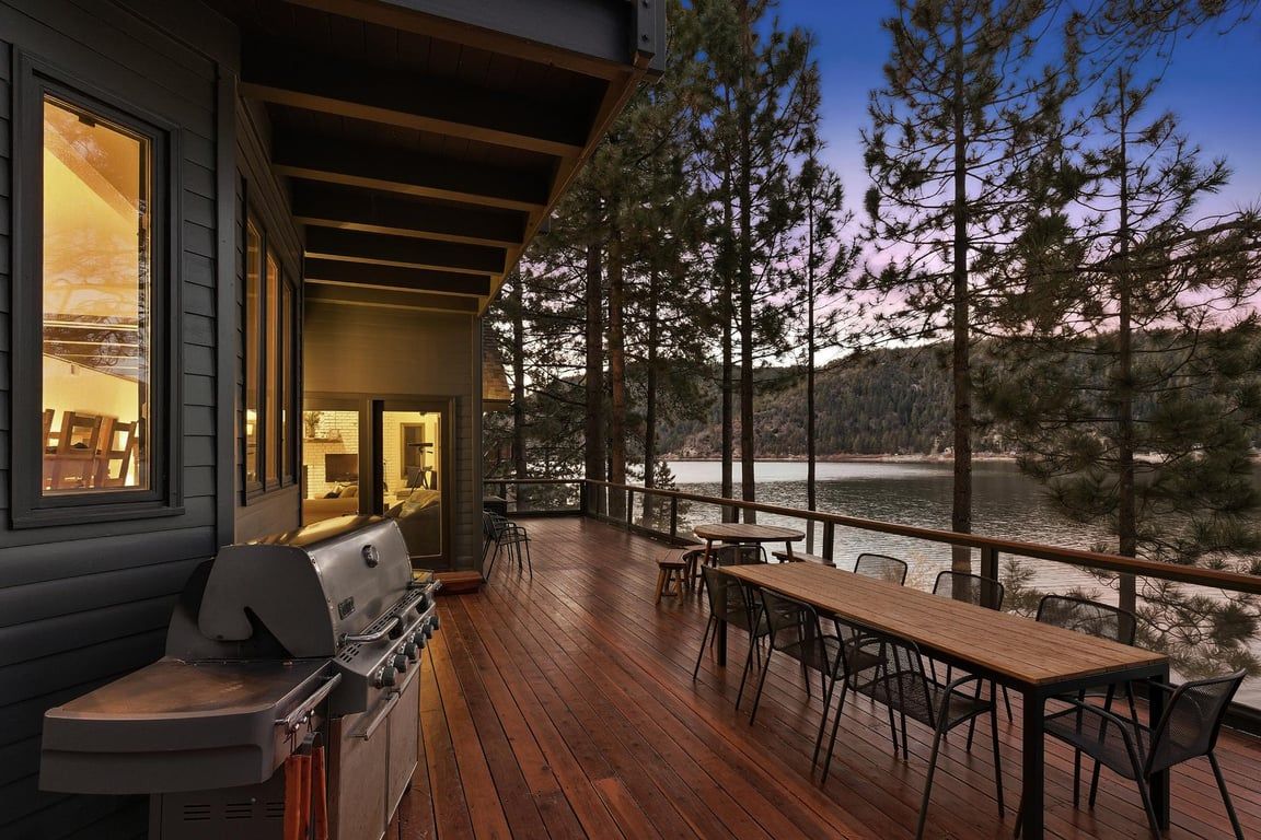 A wooden deck with a grill and dining area overlooking a lake.