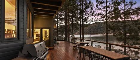 A wooden deck with a grill and dining area overlooking a lake.