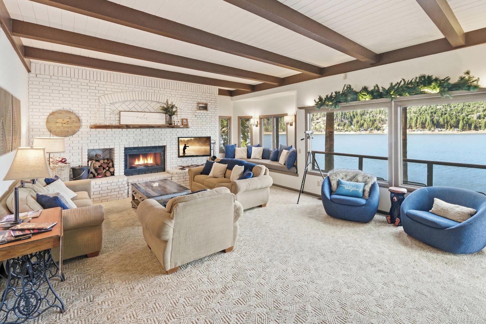 A cozy living room with a fireplace, comfortable seating, and a large window overlooking a body of water.