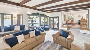 A spacious living area with a large sofa, armchairs, and a coffee table. There are large windows offering views of the outdoors.