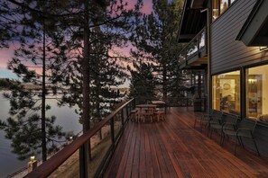 A wooden deck with outdoor seating, overlooking a lake and surrounded by tall trees.