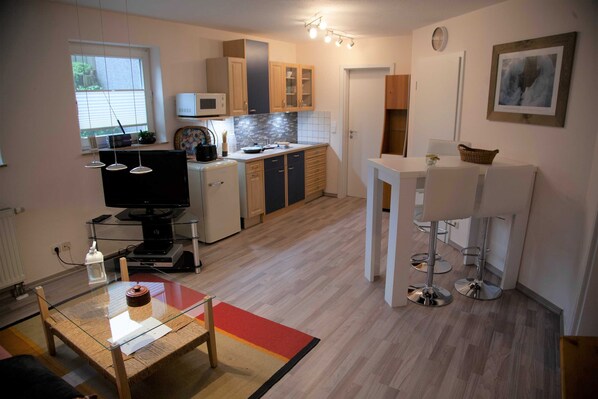 A compact kitchen with a microwave, cabinets, and a dining area with a bar stool.
