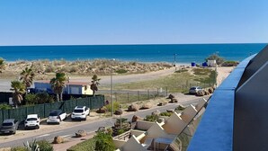 A coastal view with a road leading to a beach, parked cars, and a clear blue sky. - Cozy studio with parking in Cap d'Agde, near the sea (Cap d'Agde naturisme)