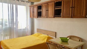 A room with a bed, a table, and wicker chairs. - Cozy studio with parking in Cap d'Agde, near the sea (Cap d'Agde naturisme)