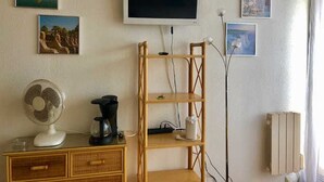 A room with a TV mounted on the wall, a fan, a coffee maker, and a radiator. - Cozy studio with parking in Cap d'Agde, near the sea (Cap d'Agde naturisme)