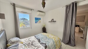 Ein Schlafzimmer mit Bett, einem Fenster mit Blick, einer Deckenleuchte und einem durch einen Vorhang einsehbarer Badezimmer.