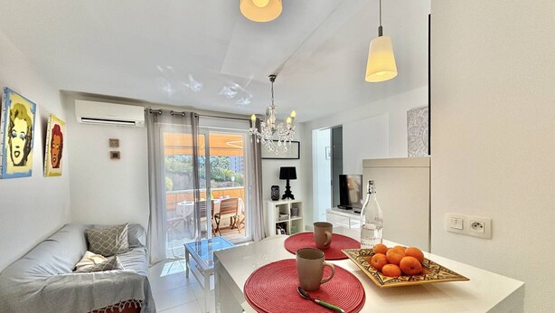 Eine moderne Küche mit einer zentralen Kochinsel, einem Essbereich mit einer Couch und Blick auf eine Terrass.'