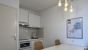 A compact kitchen with white cabinets, a tiled backsplash, a small oven, and a dining table with chairs. - 2-room apartment with terrace and parking in Banyuls-sur-Mer (Banyuls-sur-Mer)