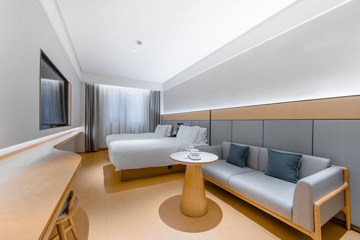 Une chambre d’hôtel moderne équipée d’un lit, d’un canapé, d’une table ronde et d’un téléviseur fixé au mur.