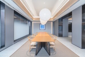 Un salón de conferencias con una mesa larga, sillas, una lámpara colgante y un cuadro en la pared.