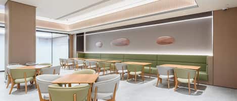 A modern interior with tables and chairs arranged in a casual dining area, a green cushioned bench, and a recessed ceiling design.
