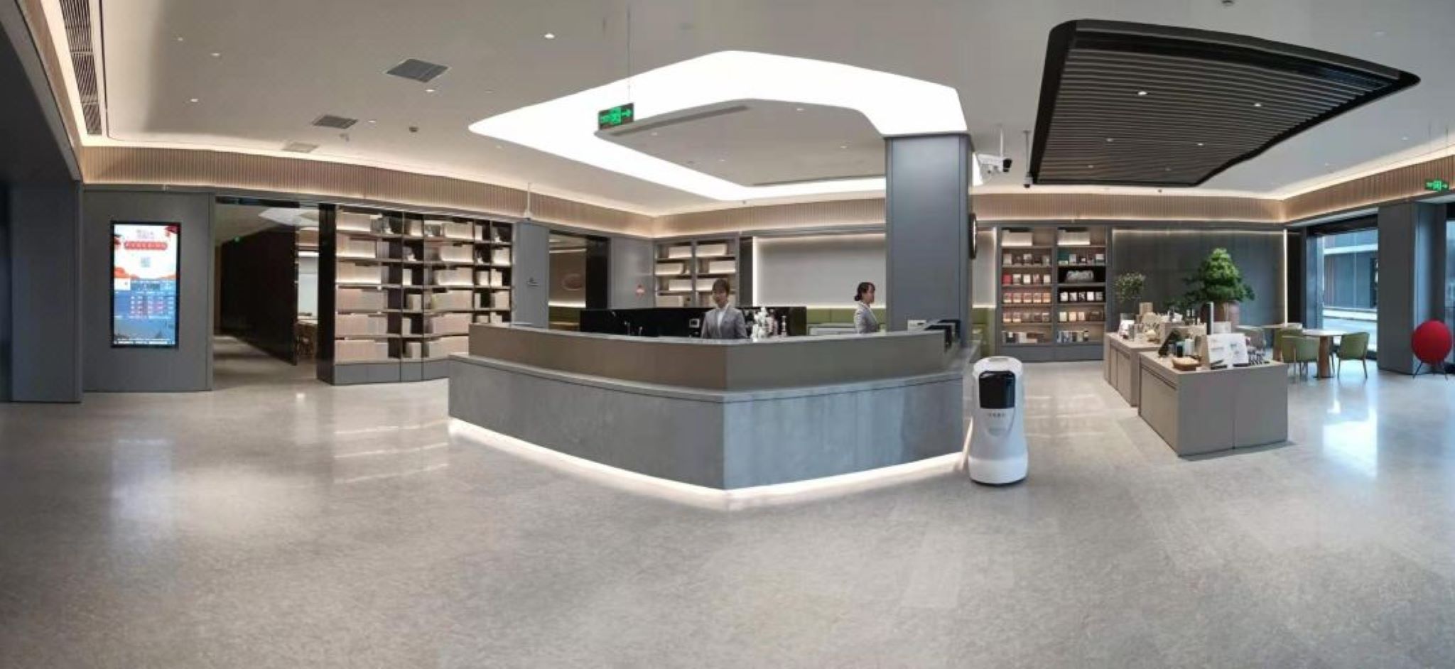 A modern lobby with a reception desk, a self-service kiosk, and a large digital display.