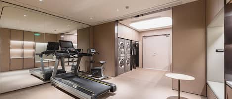 A modern hotel room with a treadmill, a small table, and a washing machine.
