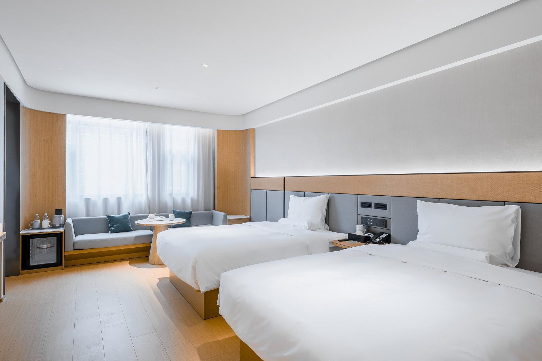 A hotel room with two beds, a sofa, a small table, and a window with curtains.