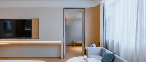 Una habitación de hotel moderna con cama, sofá, mesa de comedor y televisor montado en la pared.