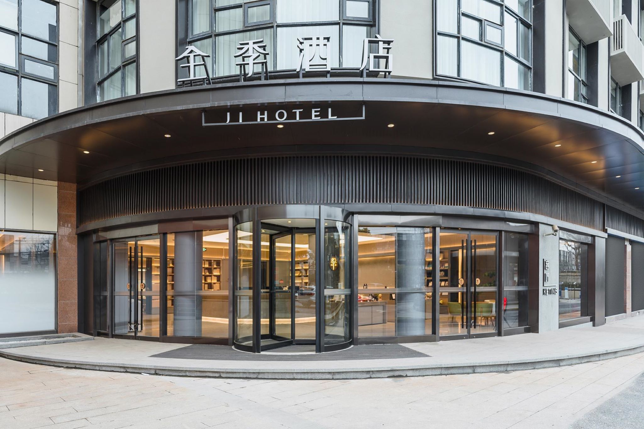 Entrada de hotel con puerta giratoria, fachada de vidrio y señalización en chino e inglés.