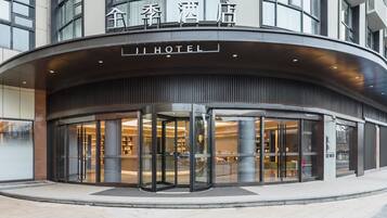 Entrada de hotel con puerta giratoria, fachada de vidrio y señalización en chino e inglés.