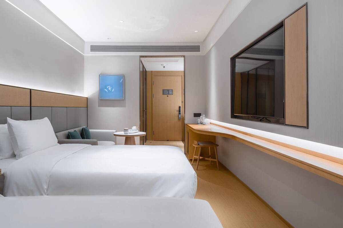 A hotel room with two beds, a desk, a chair, a TV, and a door leading to a bathroom.