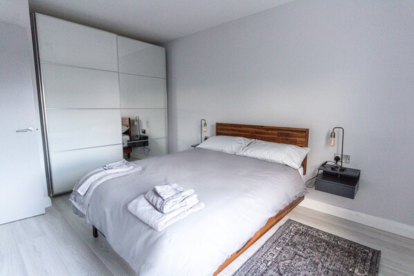 A modern bedroom with a large bed, a wooden headboard, a nightstand with a lamp, and a wardrobe. - Beach front apartment - Ballycastle beside the beach (Ballycastle)
