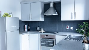 Una cocina moderna con armarios blancos, una campana extractora de acero inoxidable, horno integrado y un lavamanos.