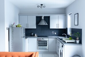 A modern kitchen with grey cabinets, a built-in oven, a sink, and a washing machine.