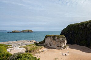A coastal landscape with rocky cliffs, a sandy beach, and calm sea.