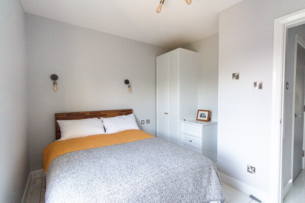 A bedroom with a bed, a wardrobe, a nightstand, and a framed picture on the nightstand.