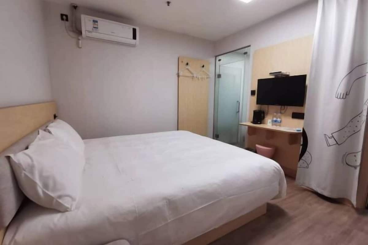 A hotel room with a bed, a TV, a desk with a chair, and a wardrobe.