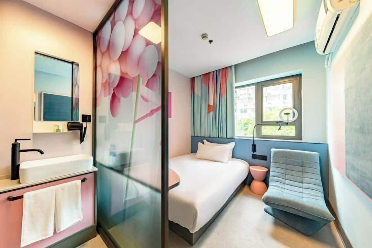 A modern hotel room with a bed, bedside table, and a glass partition.