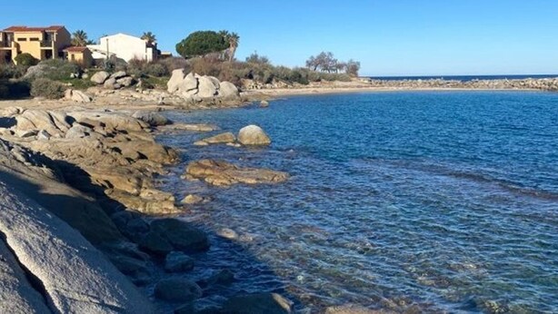A coastal scene with rocky terrain, clear blue water, and buildings in the background. - Beachfront Apartment with Terrace & Wi-Fi in Lumio, 4 Guests (Lumio)
