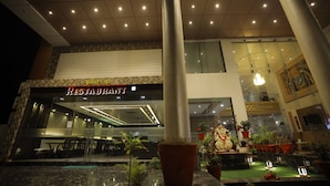 A restaurant with a modern interior, large windows, and a variety of potted plants outside. - The Grand Astoria Somnath (Veraval)