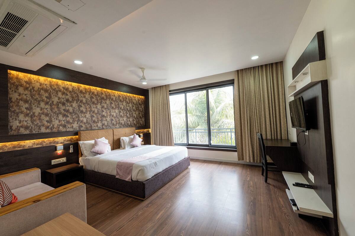Quarto de hotel moderno com uma cama grande, televisão, secretária e janela com cortinas.