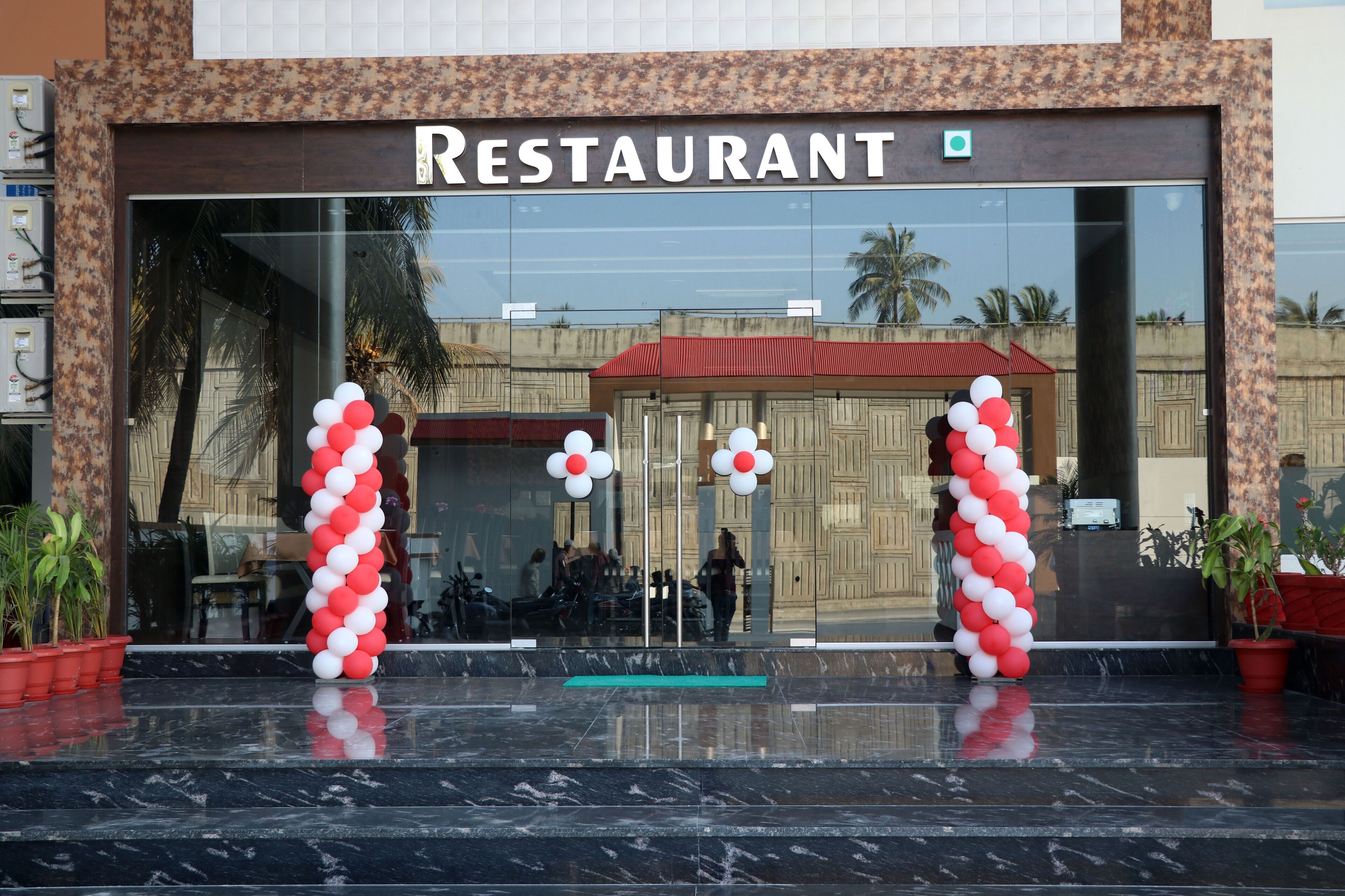 Ein Restaurant mit Glasfassade, roten und weißen Luftballons und Topfpflanzen.
