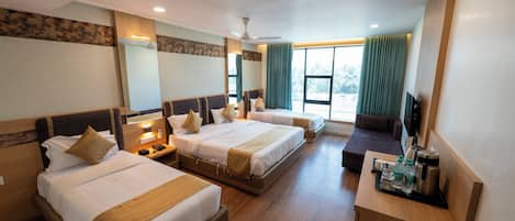 A hotel room with three beds, a desk with a coffee maker, and a TV.