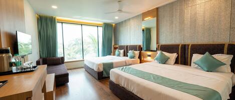 A hotel room with two beds, a desk, a sofa, a TV, and a large window with curtains.