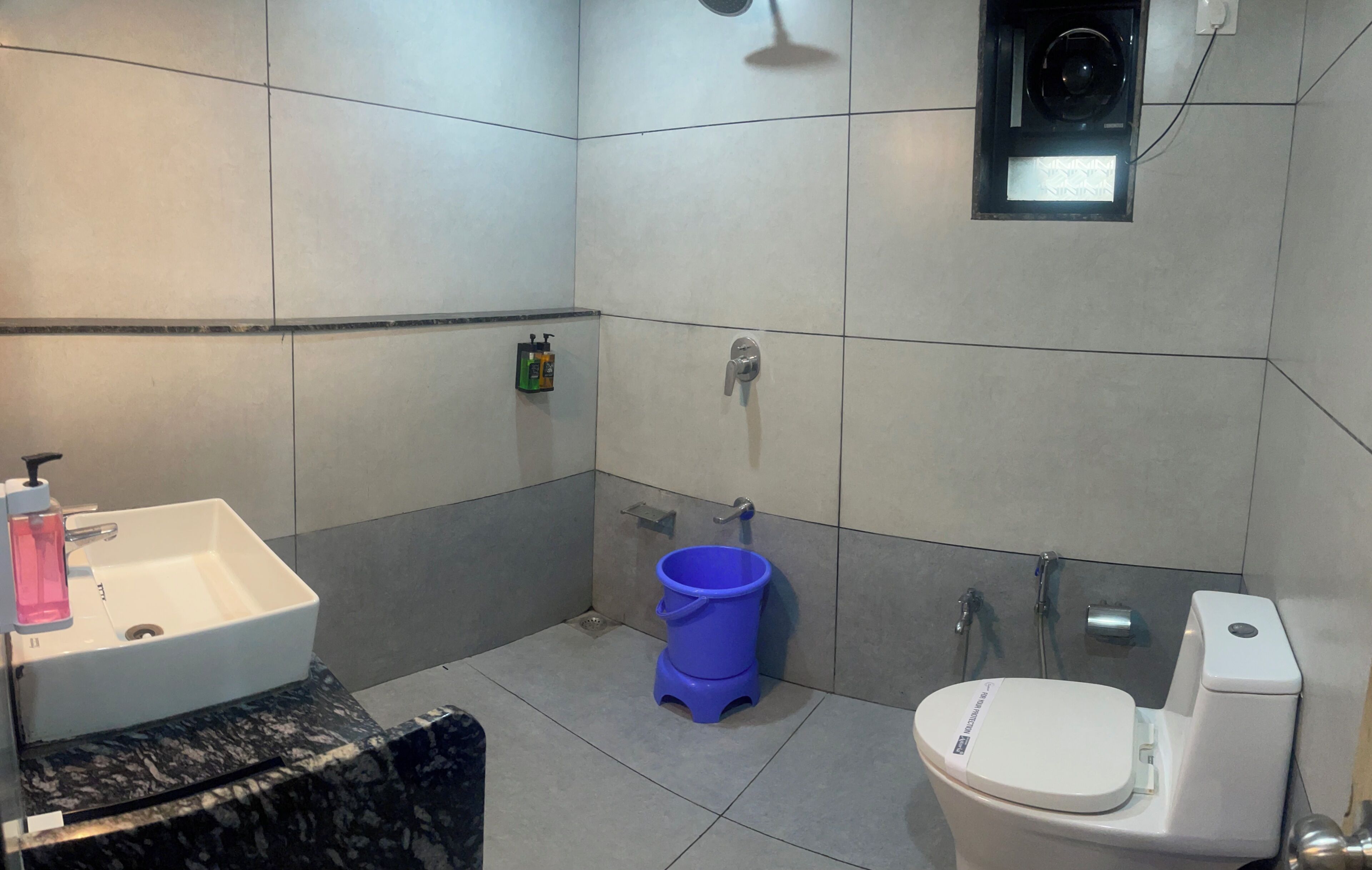 A bathroom with a sink, toilet, shower, and a blue bucket.