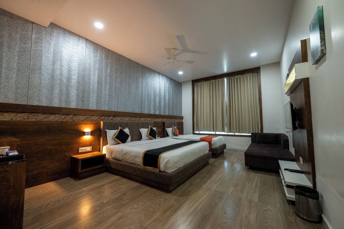 Quarto de hotel moderno com uma cama grande, um ventilador de teto, uma televisão e uma janela com cortinas.