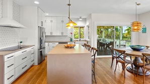 A modern kitchen with white cabinets, a central island, and a dining area with wooden chairs and a table.