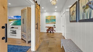 A hallway with a wooden door, a bench, a table with a vase, and artwork on the walls.