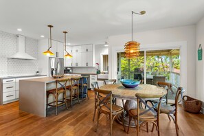 A modern kitchen with a central island, wooden chairs, and pendant lighting.