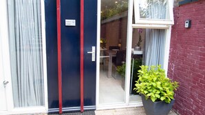 A modern building entrance with a glass door, a small indoor seating area visible through the door, and a potted plant outside. - Studio (Soesterberg)